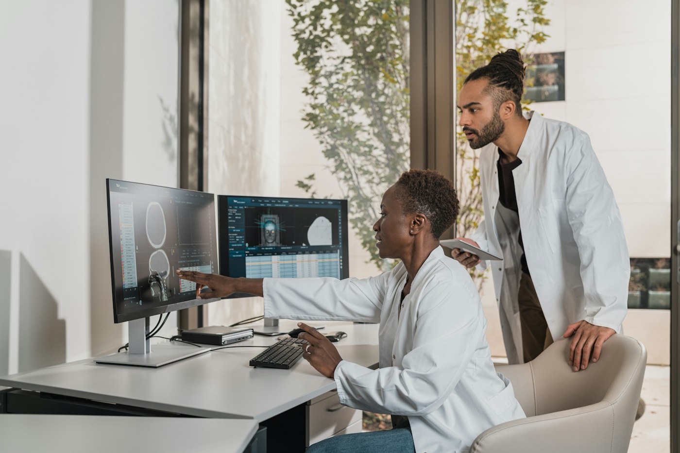 Two medical professionals reviewing scan images on computer monitors; illustrative stock photography