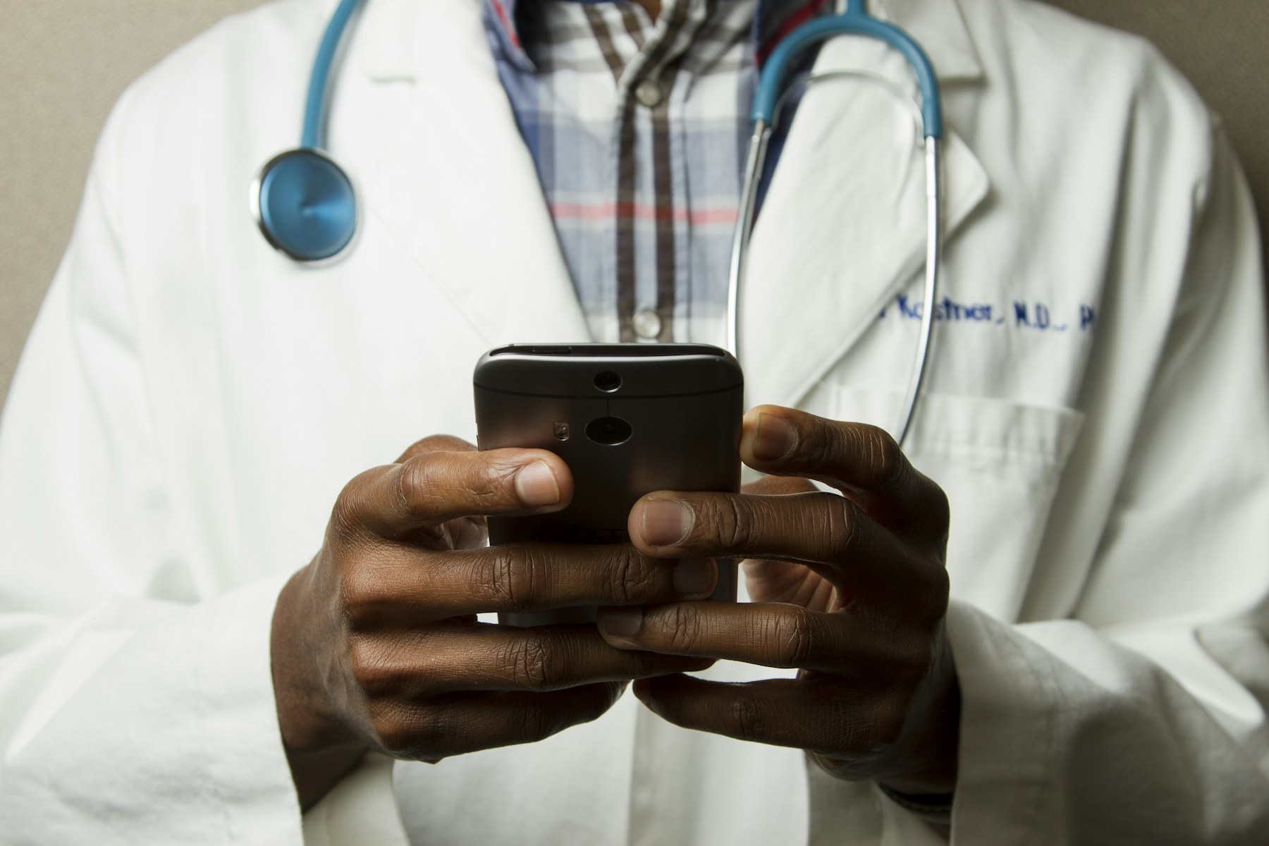 Clinician in a white coat holding a smartphone; illustrative stock photography